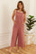 woman wearing a dusty rose sleeveless jumpsuit with pockets and wide legs, styled with a white tank top
