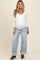 woman wearing a white long sleeve maternity top and oversized light blue jeans, showing her baby bump