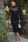 woman wearing a black fitted midi dress with sheer long sleeves and a mock neck, carrying a white handbag