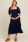 woman wearing a navy blue maternity tiered maxi dress with puff sleeves and holding her baby bump