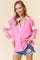 woman wearing a pink long sleeve pullover with striped collar and sleeves, paired with distressed denim shorts