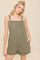 woman wearing an olive green denim overall romper with adjustable straps and side pockets