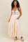 woman wearing a light beige maxi dress with black trim and adjustable straps, featuring pockets and a flowy silhouette