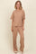 woman wearing a beige oversized t-shirt and matching wide-leg pants, standing against a neutral background