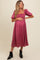 woman wearing a dark pink maternity dress with puff sleeves and a gathered bodice, gently holding her baby bump