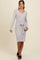 woman wearing a light gray long sleeve sweater dress with a tie waist detail and side slit, standing and smiling