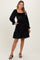 woman wearing a black smocked long sleeve dress with a tiered skirt and pockets, styled with strappy black heels