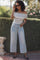 woman wearing a striped off-the-shoulder top and light wash wide-leg jeans, sunglasses on, standing outdoors