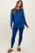 woman wearing a blue long sleeve maternity top and matching leggings, showing her baby bump, paired with cozy slippers