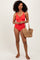 woman wearing a red one-piece swimsuit with a keyhole detail, holding a straw handbag and wearing sandals