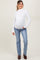 woman wearing a white long sleeve maternity top and blue jeans, showcasing her baby bump