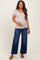 woman wearing a light taupe ribbed maternity top and blue wide-leg jeans, holding her baby bump