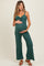 woman wearing a dark green ribbed maternity jumpsuit and gently holding her baby bump