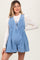woman wearing a light blue maternity denim romper with pleated detailing and a tie front