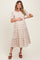 woman wearing a beige and brown plaid maternity dress with tiered hem and holding her baby bump