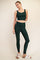 woman wearing a dark green sports bra and matching high-waisted leggings, standing with one hand on her hip