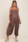 woman wearing a brown maternity jumpsuit with smocked bodice and adjustable straps, showcasing her baby bump