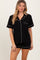 woman wearing a black short sleeve pajama set with white piping and a pocket