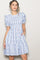 woman wearing a white short sleeve dress with blue floral pattern and puff sleeves, standing with one hand on her hip