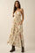 woman wearing a cream floral maxi dress with a halter neckline and side slits, paired with brown heeled boots