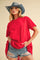 woman wearing a red oversized t-shirt and distressed denim shorts, accessorized with a blue cowboy hat