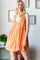 woman wearing an orange sleeveless dress with a deep V-neck and tie detail, posing with a playful expression