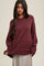 woman wearing a maroon oversized knit sweater with a rounded neckline and ribbed hem, styled with a flowy skirt
