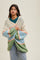 woman wearing a chunky knit cardigan in cream, blue, green, and peach with a relaxed fit over a green top and jeans