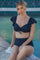 woman wearing a black ruffled bikini top and high-waisted bikini bottom, sitting by the water