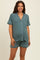 woman wearing a teal maternity sleep set with short sleeves, shorts, and white piping, showing her baby bump