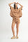 woman wearing a beige oversized top with matching drawstring shorts and slide sandals, posing with hands raised.