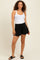 woman wearing a white tank top and black maternity shorts, standing in a relaxed pose