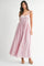 woman wearing a light pink maxi dress with adjustable straps and ruffle details, standing on a plain background