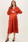 woman wearing an orange maternity midi dress with long sleeves and a tiered hem, holding her baby bump