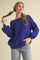 woman wearing a purple oversized ribbed sweater with off-the-shoulder neckline and balloon sleeves paired with light denim jeans