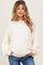 woman wearing a cream oversized maternity sweater with ribbed texture and balloon sleeves, smiling and posing with hands in pockets