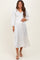 woman wearing a white pleated maternity dress with a v-neck and balloon sleeves, showing her baby bump