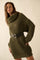 woman wearing an olive green oversized knit sweater dress with a cowl neck and black belt, posing confidently