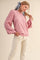 woman wearing a pink sweater with pleated sleeves and a bow in her hair, paired with white jeans