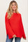 woman wearing a red oversized knit maternity sweater with side slits and long sleeves, smiling at the camera