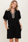woman wearing a black puff sleeve dress with a plaid neckline and side pockets