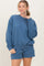 woman wearing a blue oversized sweatshirt with matching shorts, smiling at the camera