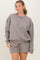 woman wearing a gray oversized sweatshirt and matching shorts, smiling at the camera