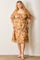 woman wearing a beige plus-size dress with floral embroidery and puff sleeves, standing against a wall