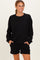 woman wearing a black oversized sweatshirt and matching black shorts, posing with hands in pockets