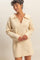woman wearing a cream-colored sweater dress with a wide collar and long sleeves, smiling softly