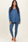 woman wearing a blue long sleeve v-neck top and matching leggings, standing barefoot against a neutral background