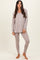 woman wearing a taupe long sleeve loungewear top and matching leggings, standing barefoot on a light background