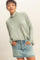 woman wearing a light green long sleeve turtleneck top and a denim mini skirt, posing with hands in pockets