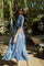woman wearing a blue tiered maxi dress with short sleeves, standing outdoors among greenery